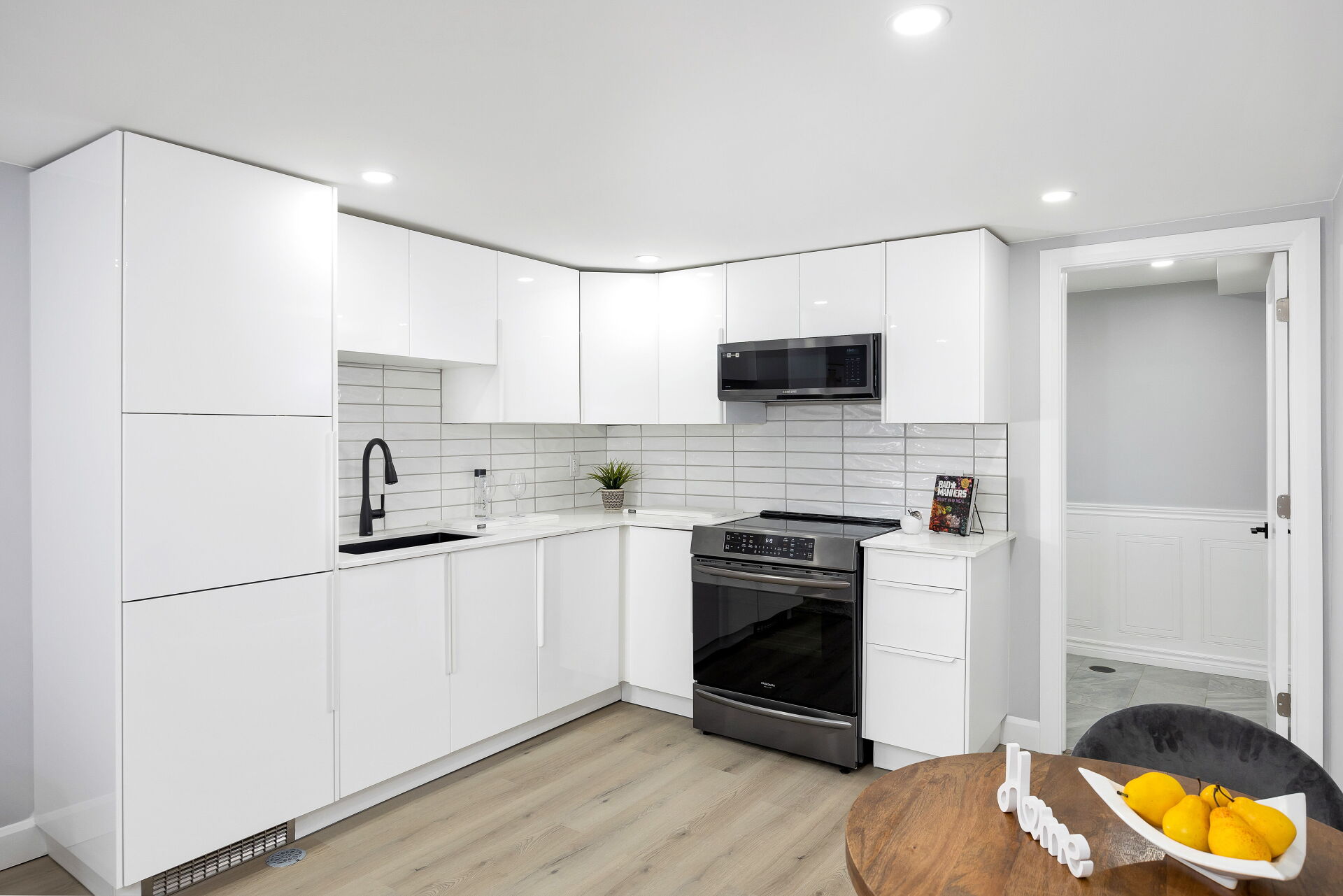 Modern white kitchen with black sink, full-size range and over-the-range microwave.