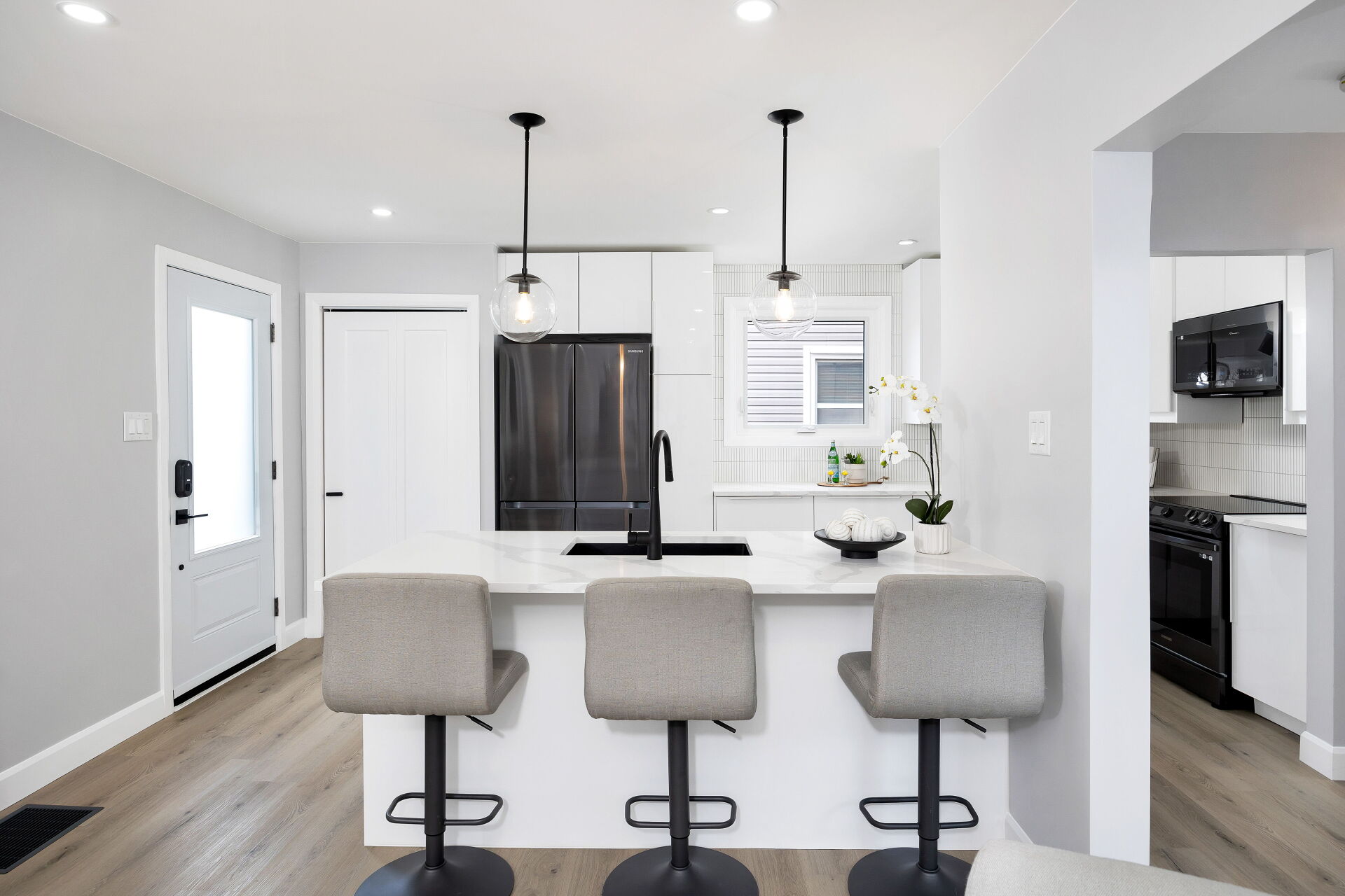 Kitchen breakfast bar with quartz counter, black undermount sink and glass pendant lights.