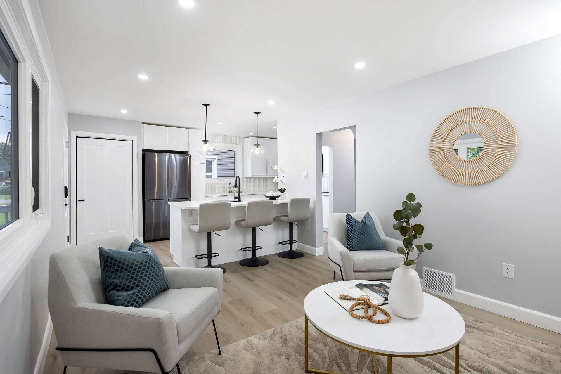 Bright upper-unit living room opening onto a white kitchen with a breakfast bar and three stools.